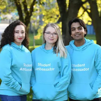 three student ambassadors standing in a park and smiling
