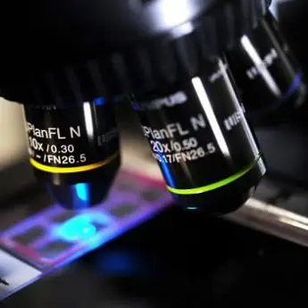 Close-up of microscope objectives over a slide with a blue light shining through