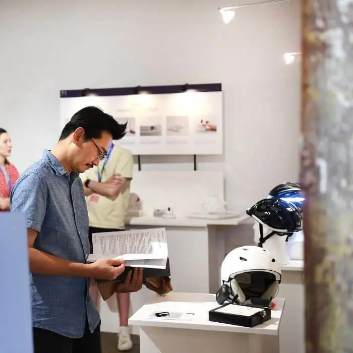 Person reading a book at a tech exhibition with products displayed in the background.