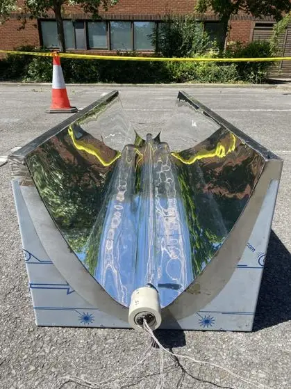 A reflective aluminium parabolic dish sits on a paved area, with a connector at the base.