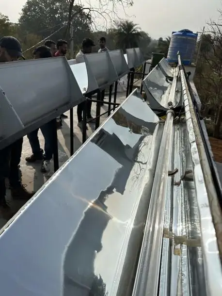 A row of reflective metal troughs on a rooftop, surrounded by trees and a water tank in the background.