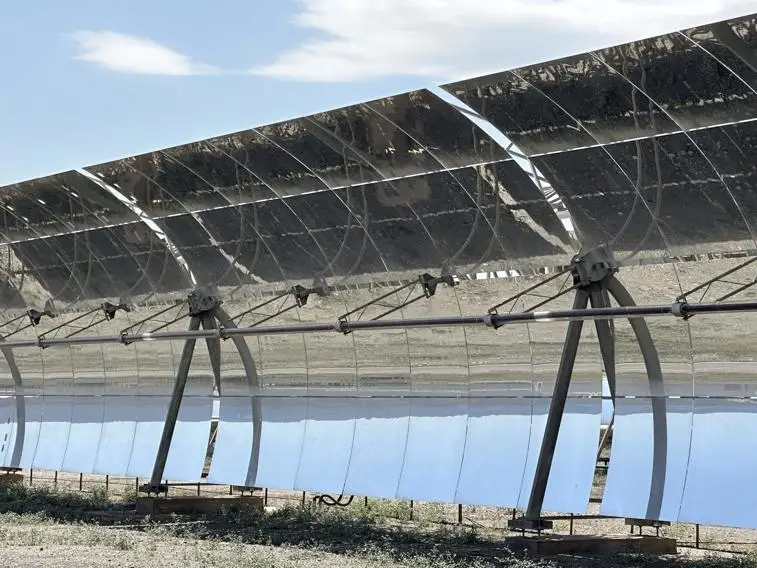 A row of reflective solar panels with a mechanical support structure, capturing sunlight against a clear blue sky.