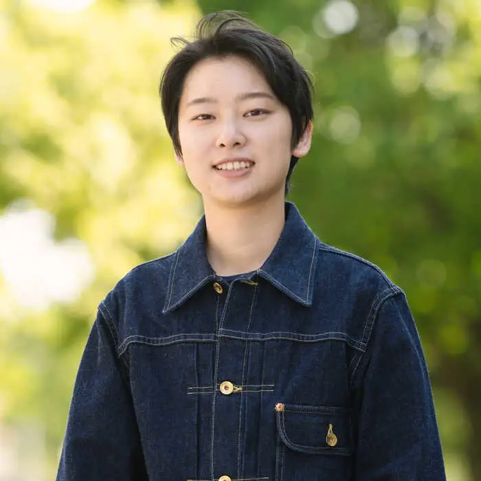 Person in a denim jacket standing in front of a blurred green background.