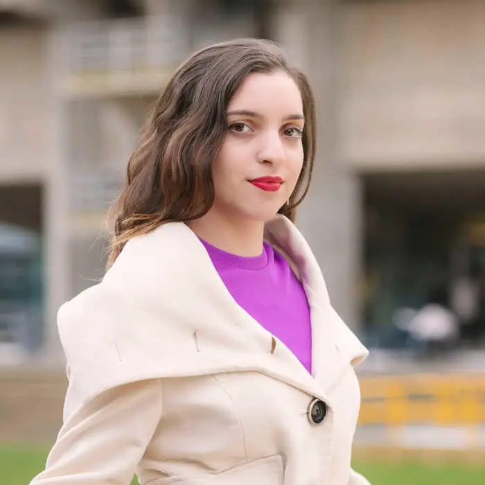 A person in a white coat and purple top standing outdoors.