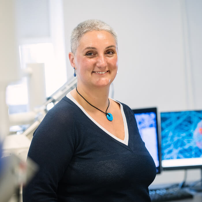 portrait photo of dr lorna anguilano in a lab with monitors displaying scientific images in the background.