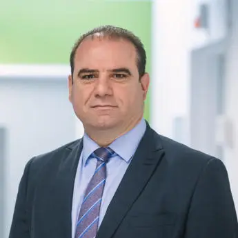 Portrait photo of Professor Hussam Jouhara, a man in a dark suit, light blue shirt, and patterned blue tie, standing indoors.