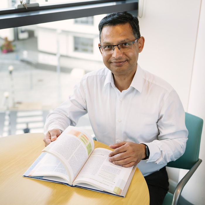 Subhash Pokhrel, a man in a white shirt reading a book at a table indoors