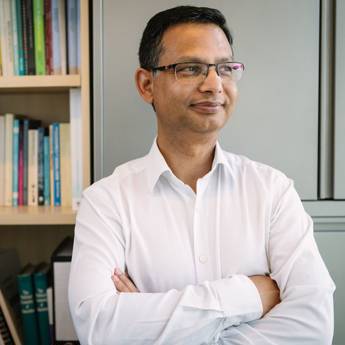 Subhash Pokhrel a man in white shirt with arms crossed, standing before a bookshelf.