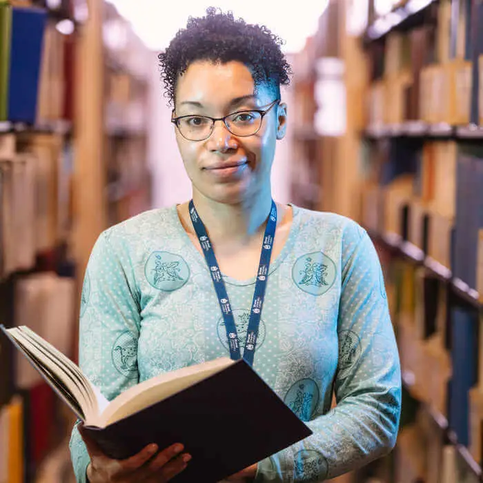 student with a book standing between bookshelves