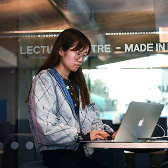 female students working on a laptop in front of the Brunel Lecture Centre