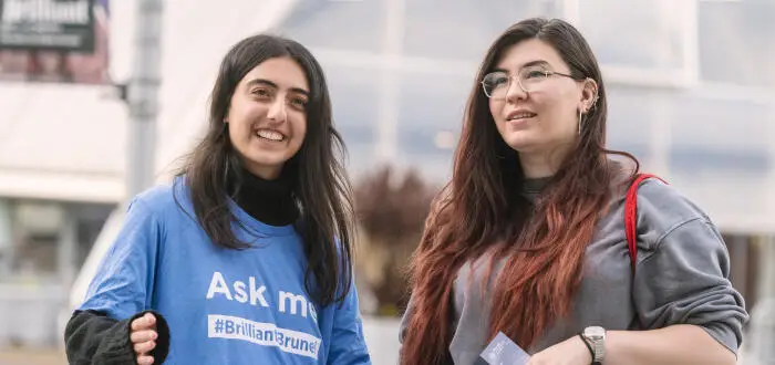 Two women standing outdoors one wearing a blue Ask me t-shirt