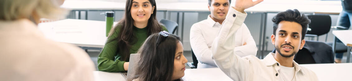 A classroom setting with students engaged in discussion one student raises their hand to contribute while others listen attentively.