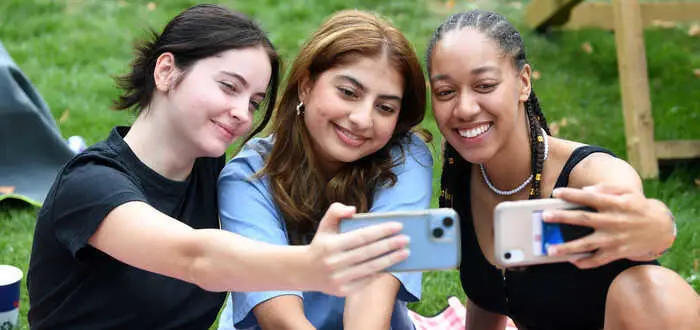 Three people taking a selfie with a smartphone in a grassy area